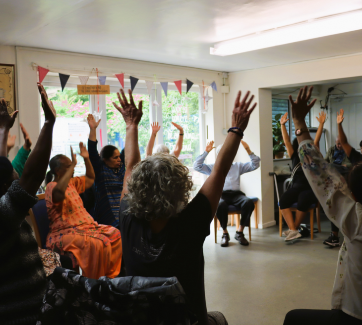 A group of adults sat down in a room with their arms in the air